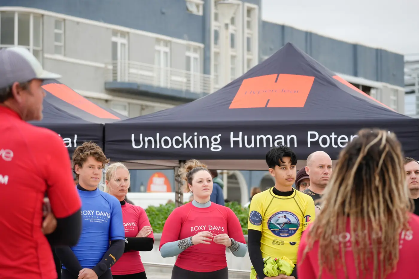 Roxy Davis Foundation team and young adaptive surf therapy participants gathering beneath an Unlocking Human Potential banner in Cape Town, supported by Raise for a Child.